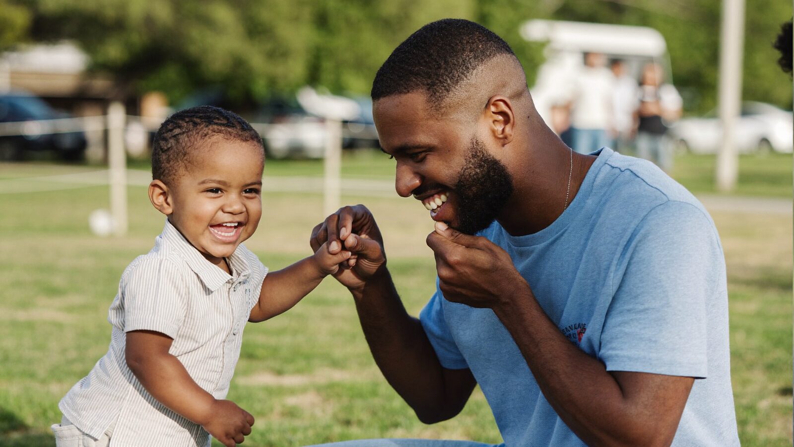 Father in his 30s laughing with his toddler son in a park