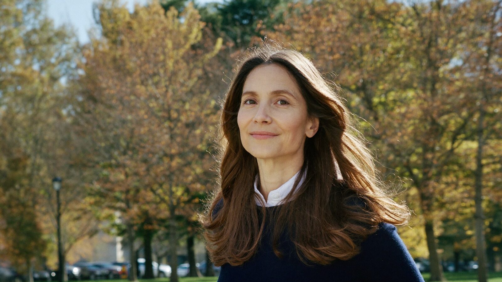 Woman in her 40s with long brown hair walking through a park in autumn