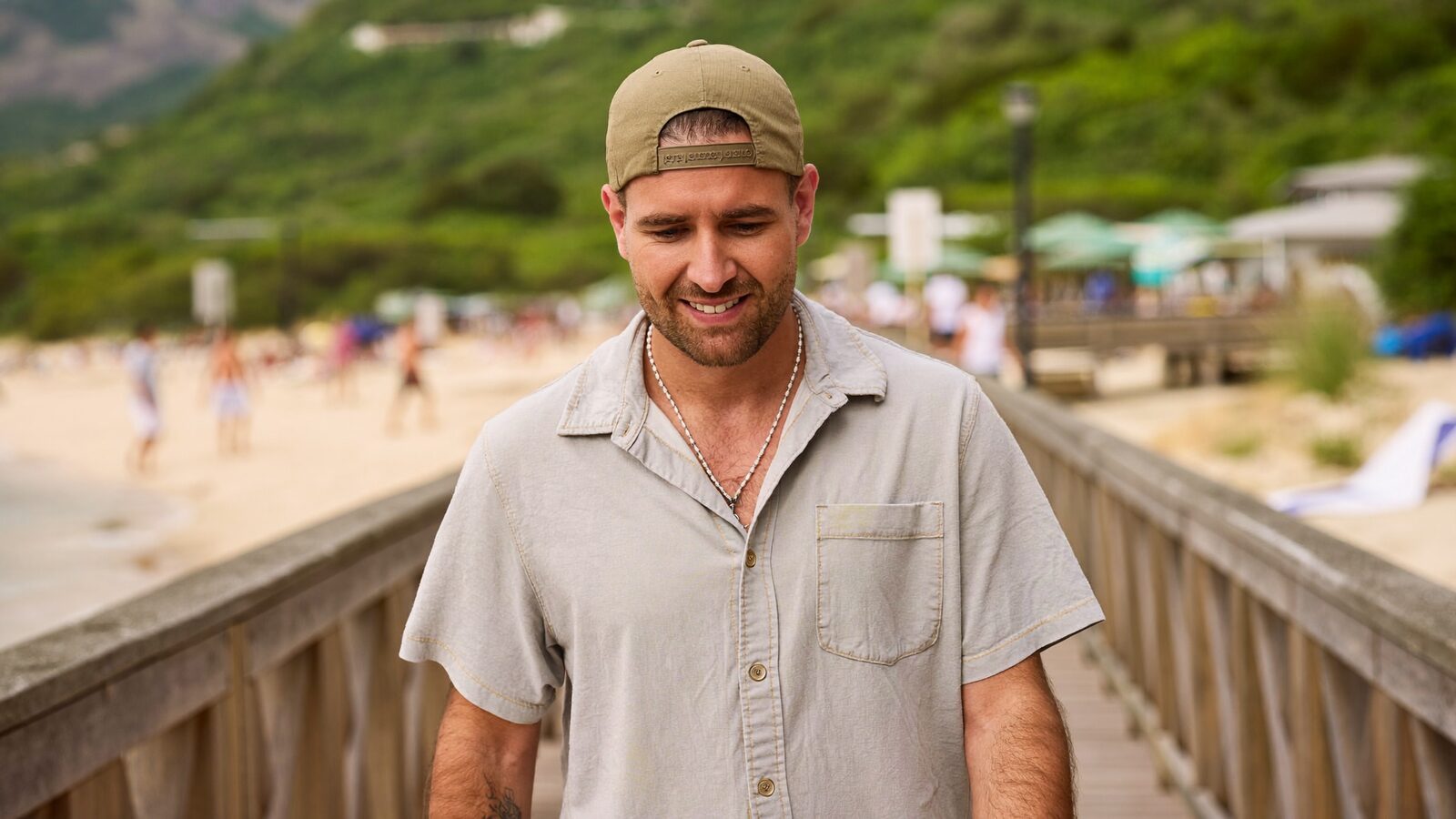 Man in a loose baseball cap walking along a beach boardwalk in summer