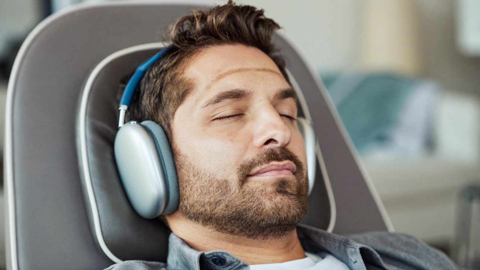 Man in his 40s relaxing in a reclining armchair with headphones on, eyes closed and comfortable