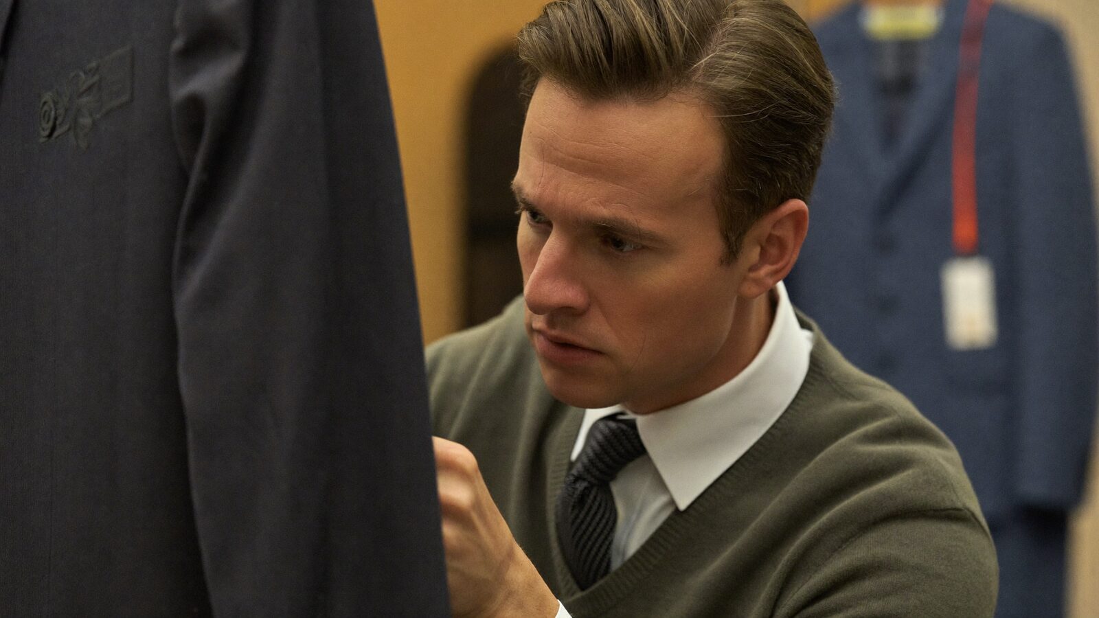 Man in his 30s closely inspecting a suit jacket in a tailor's shop