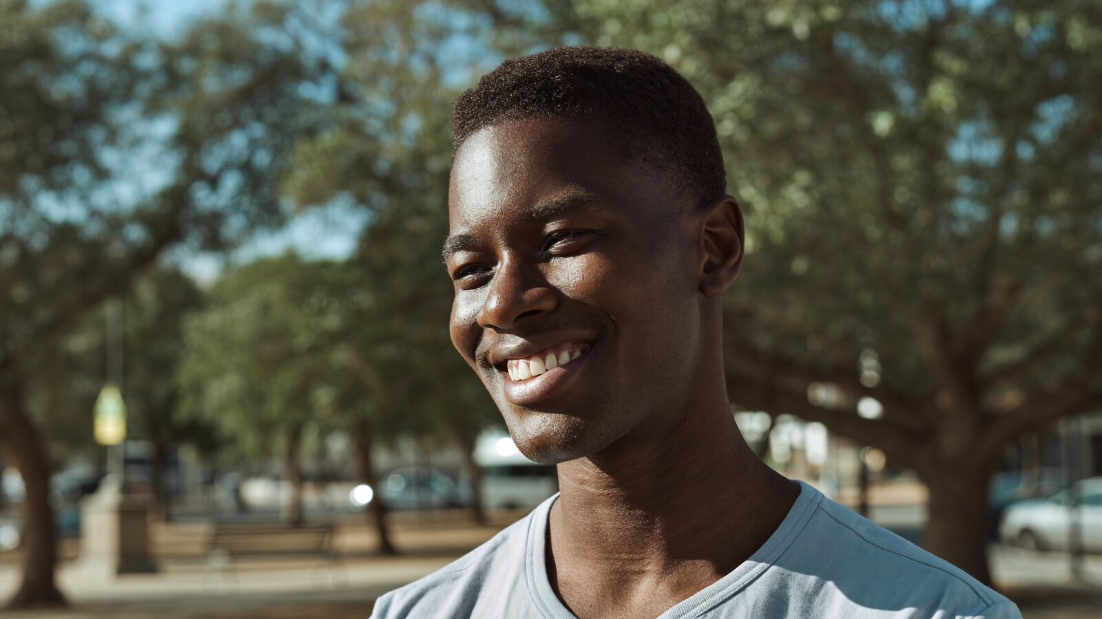 Man in his 30s with short natural Afro-textured hair smiling outdoors in a park
