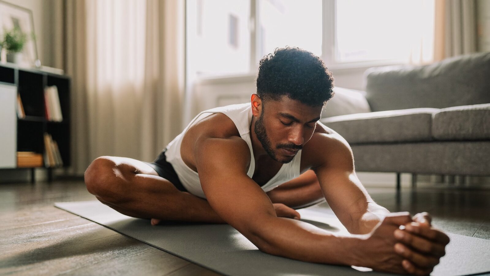 Man in his 40s stretching on a yoga mat in a bright living room