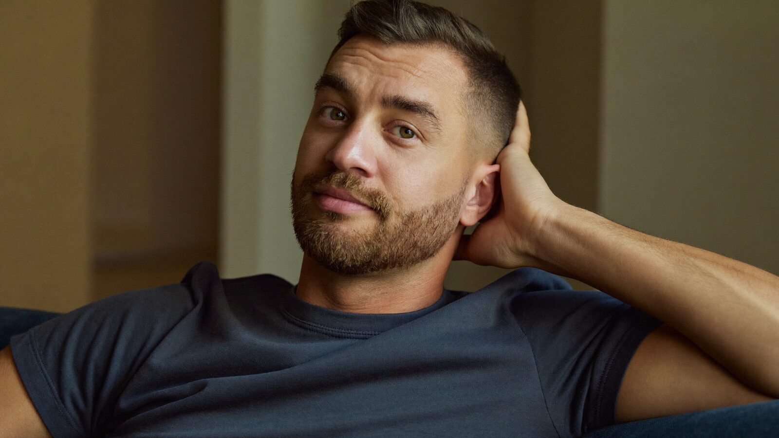 Man in his 30s with a short trimmed beard relaxing on a sofa at home