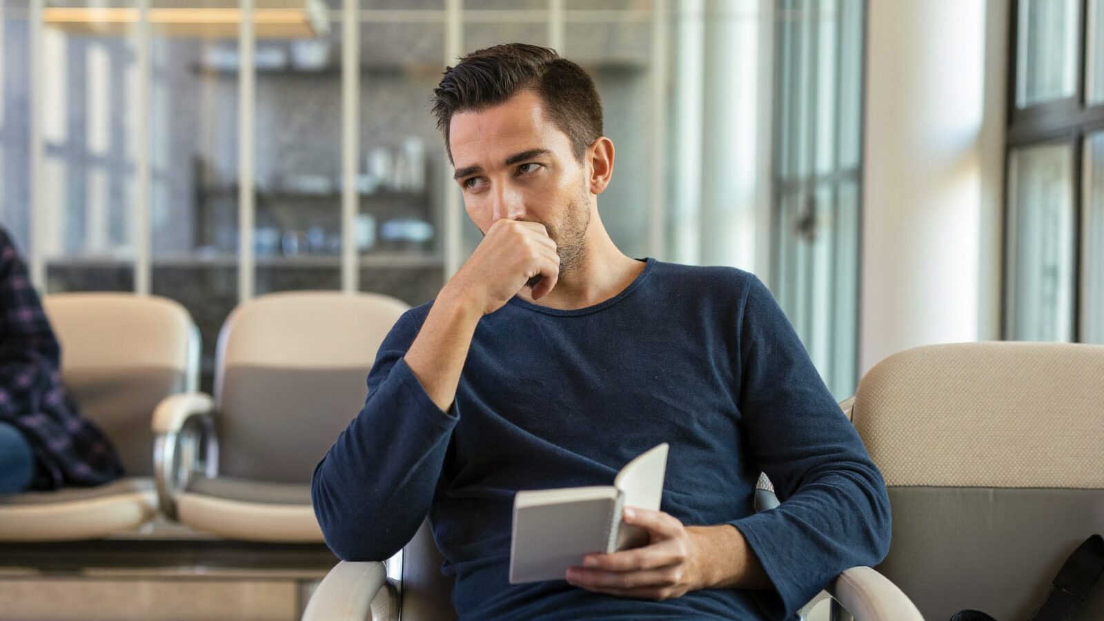 Man in his 40s in a bright waiting room holding a small notebook, ready for a consultation