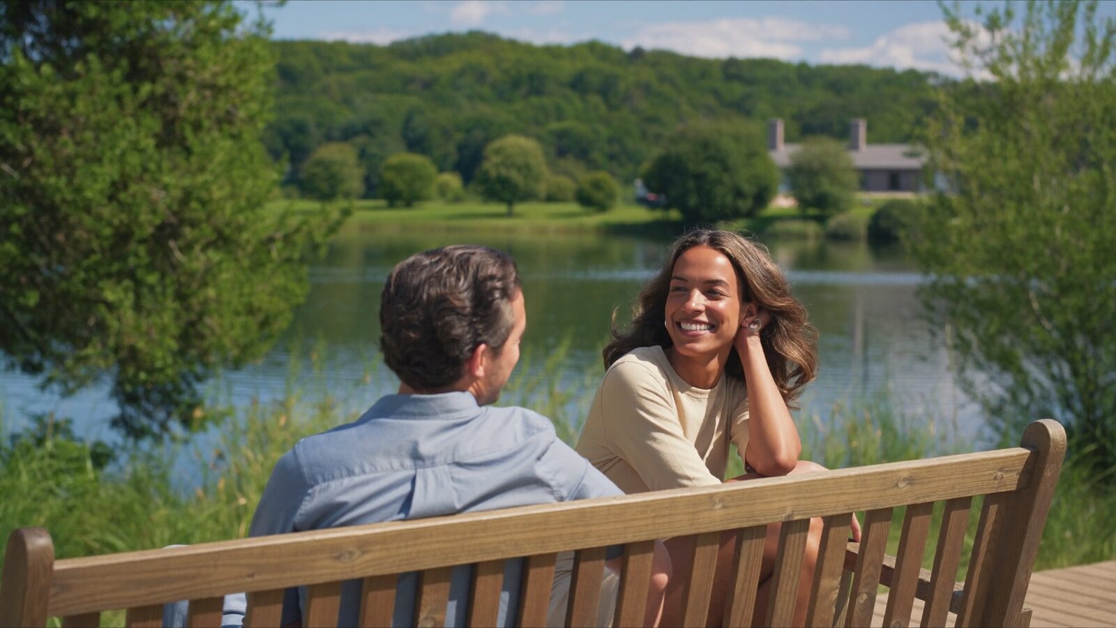 Man and woman in their 40s chatting and laughing on a bench by a lake