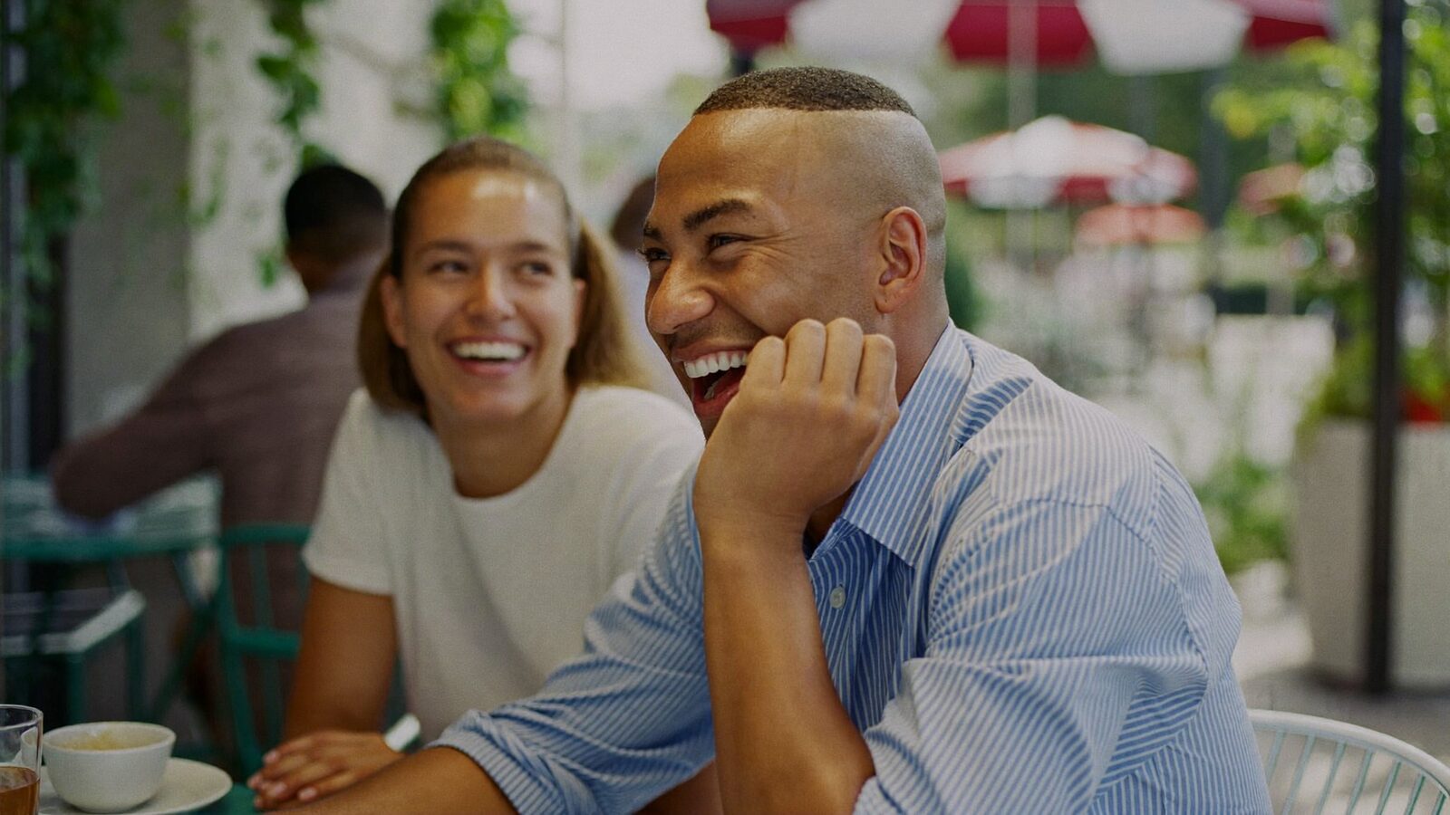 Two friends laughing together at an outdoor cafe table on a sunny afternoon